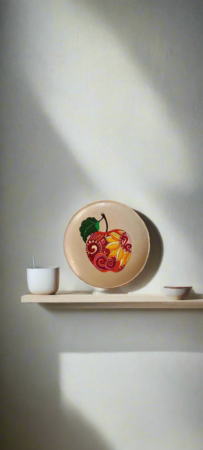 Paint tubes arranged around a plate with a painted apple design on a white fabric background